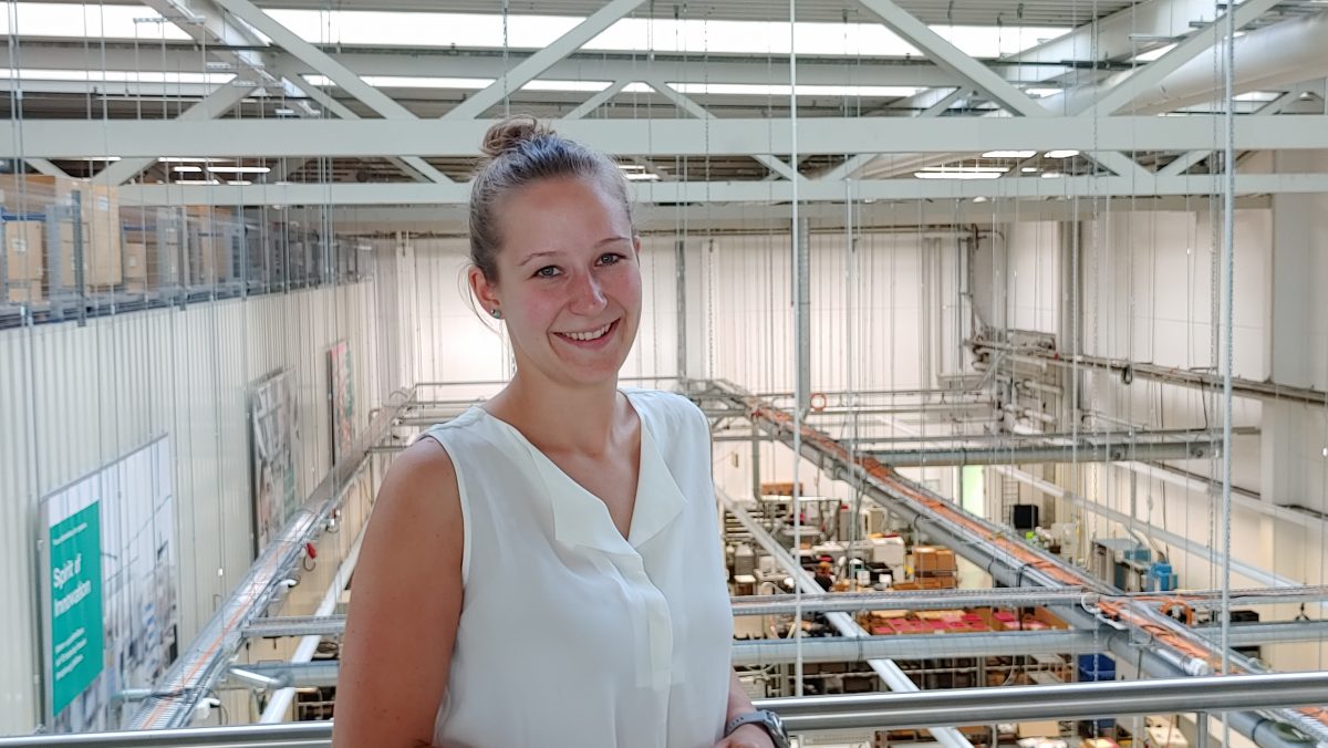 Emma leans against a balustrade. Behind her you have a view of a Pepperl+Fuchs warehouse.