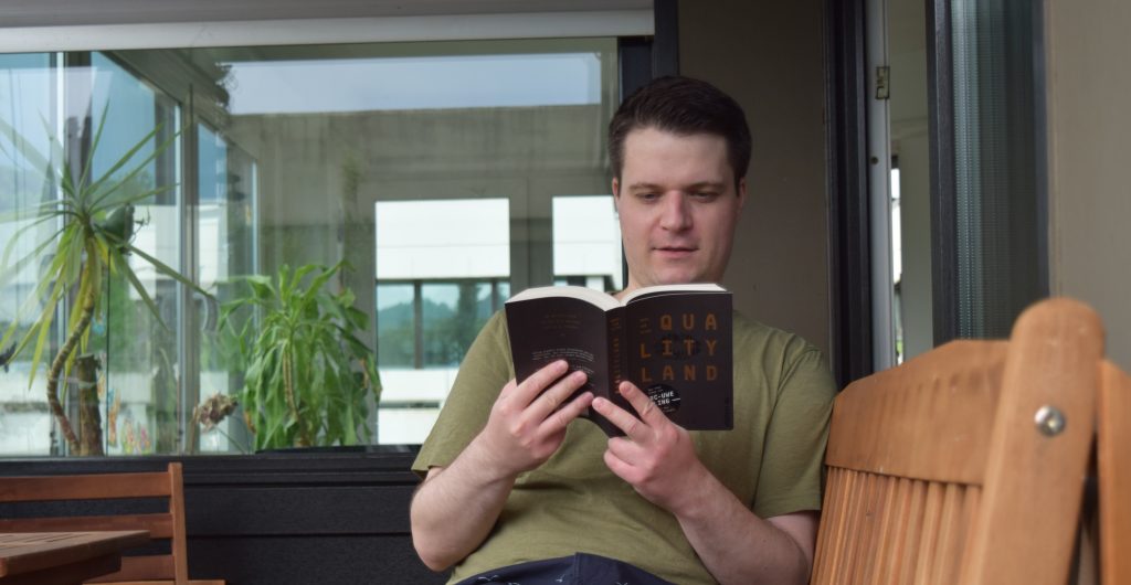 Matthias sits on his balcony and reads the book “Qualityland”.