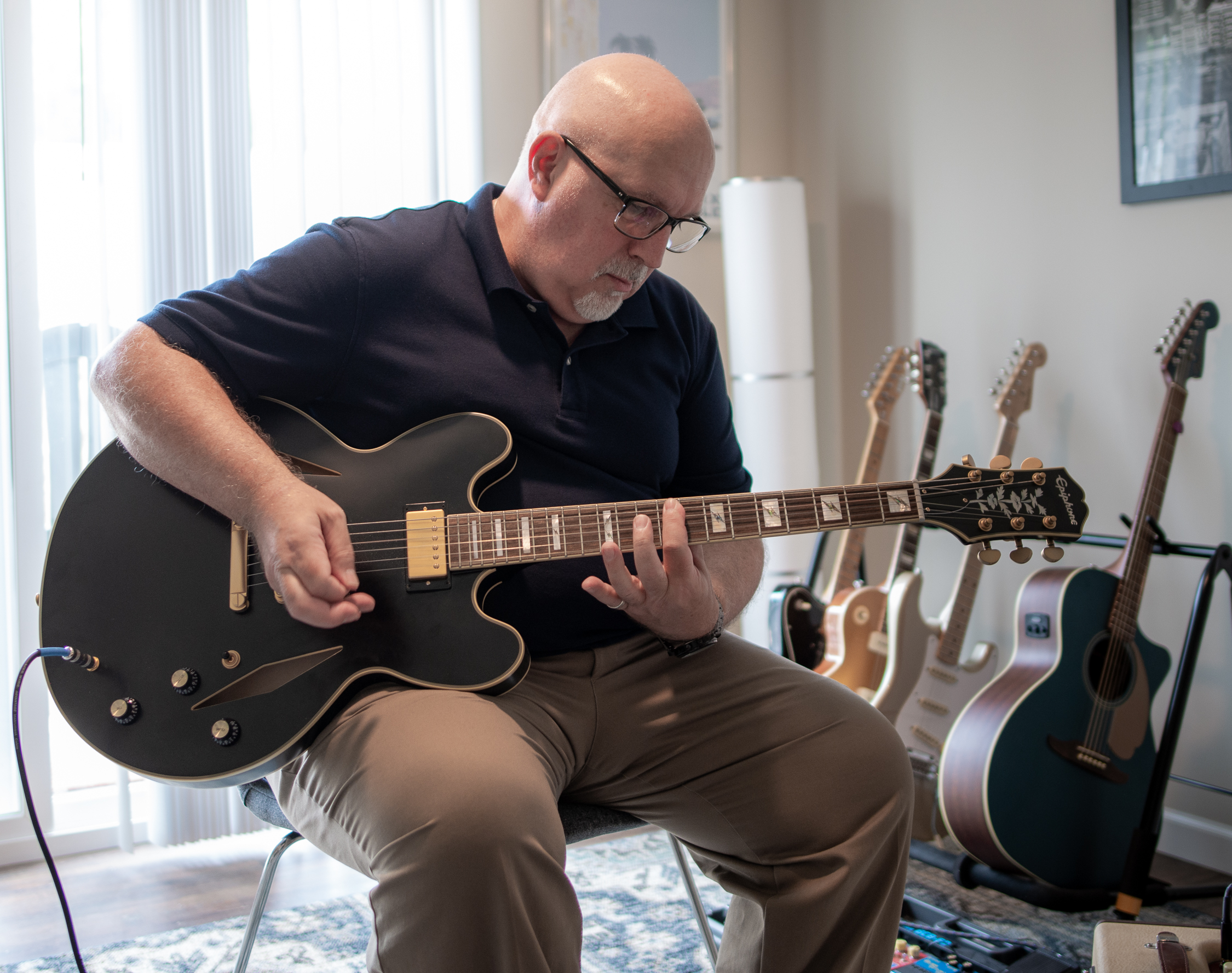 Andrew, Sales Performance Coach, sits on a chair and plays the guitar.