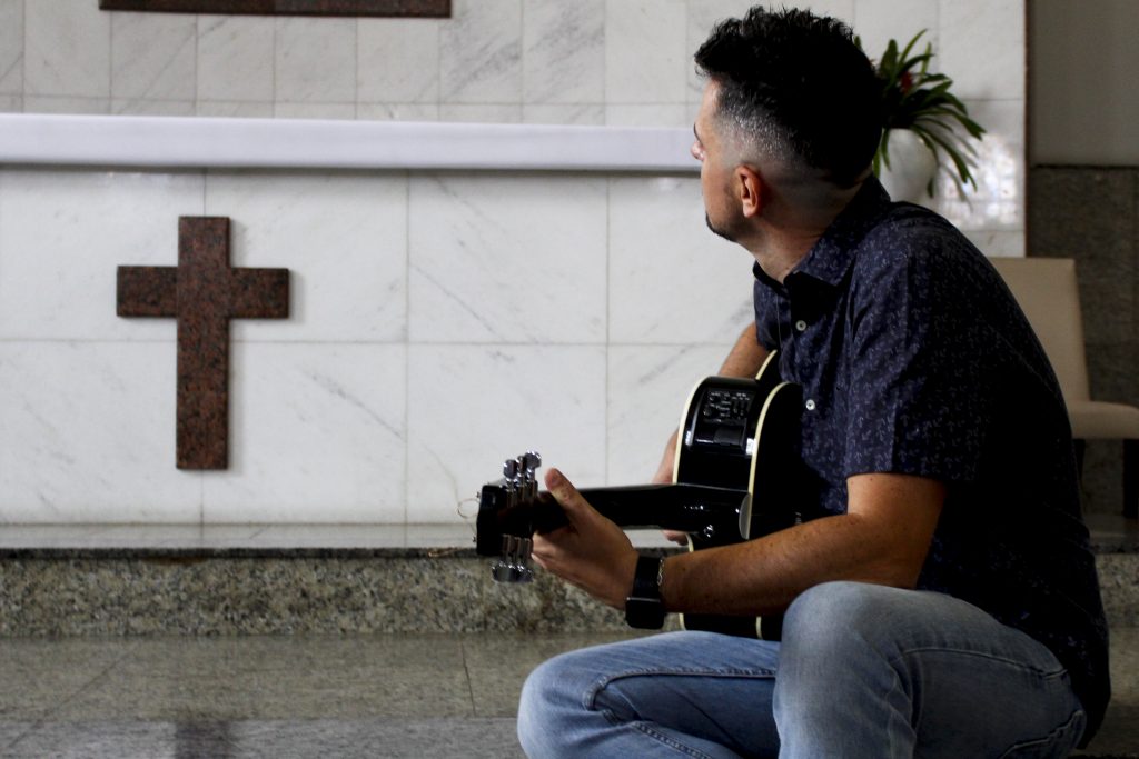 Dênis, sits on the floor of a church and plays the guitar.