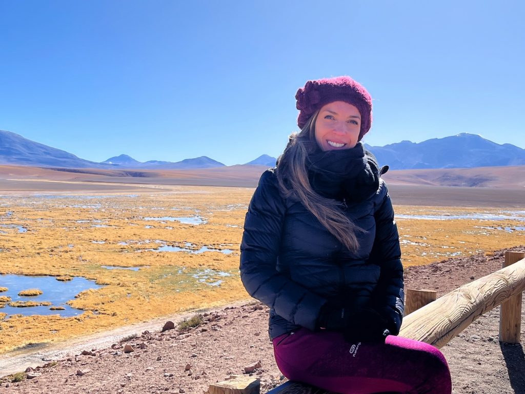 In this picture you can see Carina in the Atacama Desert in Chile. She sits on a wooden barrier and smiles into the camera.