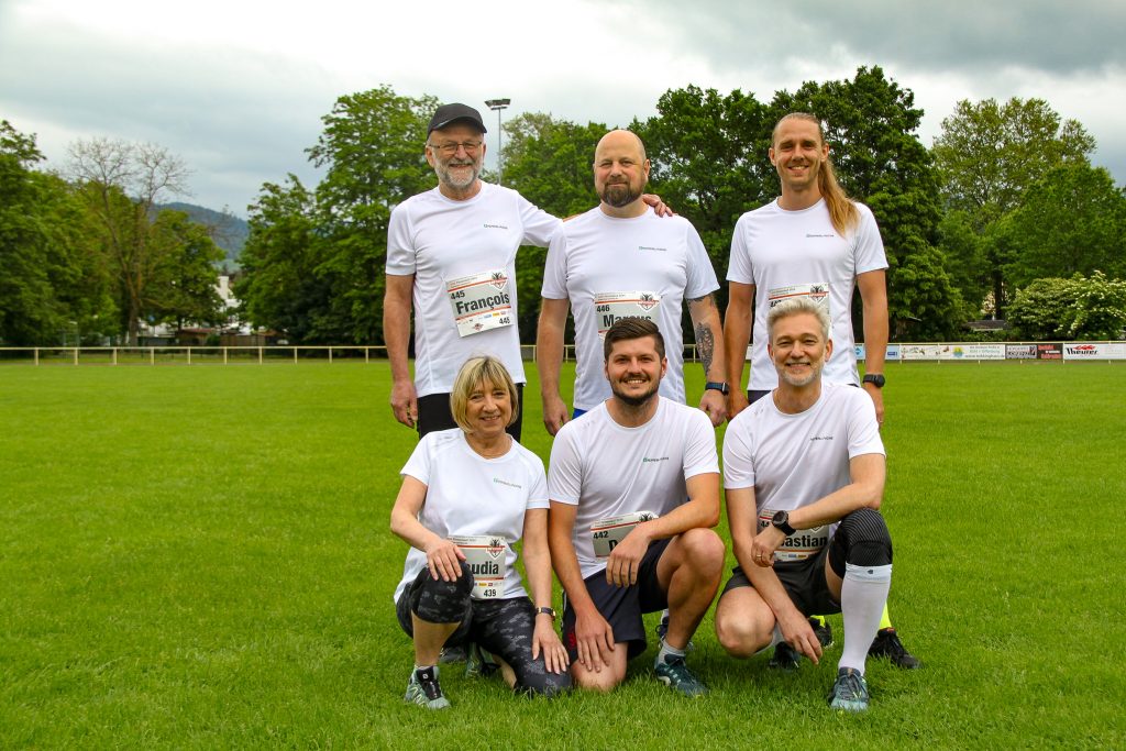 Group photo of the Pepperl+Fuchs runners at the company run in Bühl. They are on a sports field, three of them standing, the other three kneeling in front of them. They wear the white Pepperl+Fuchs running shirts.