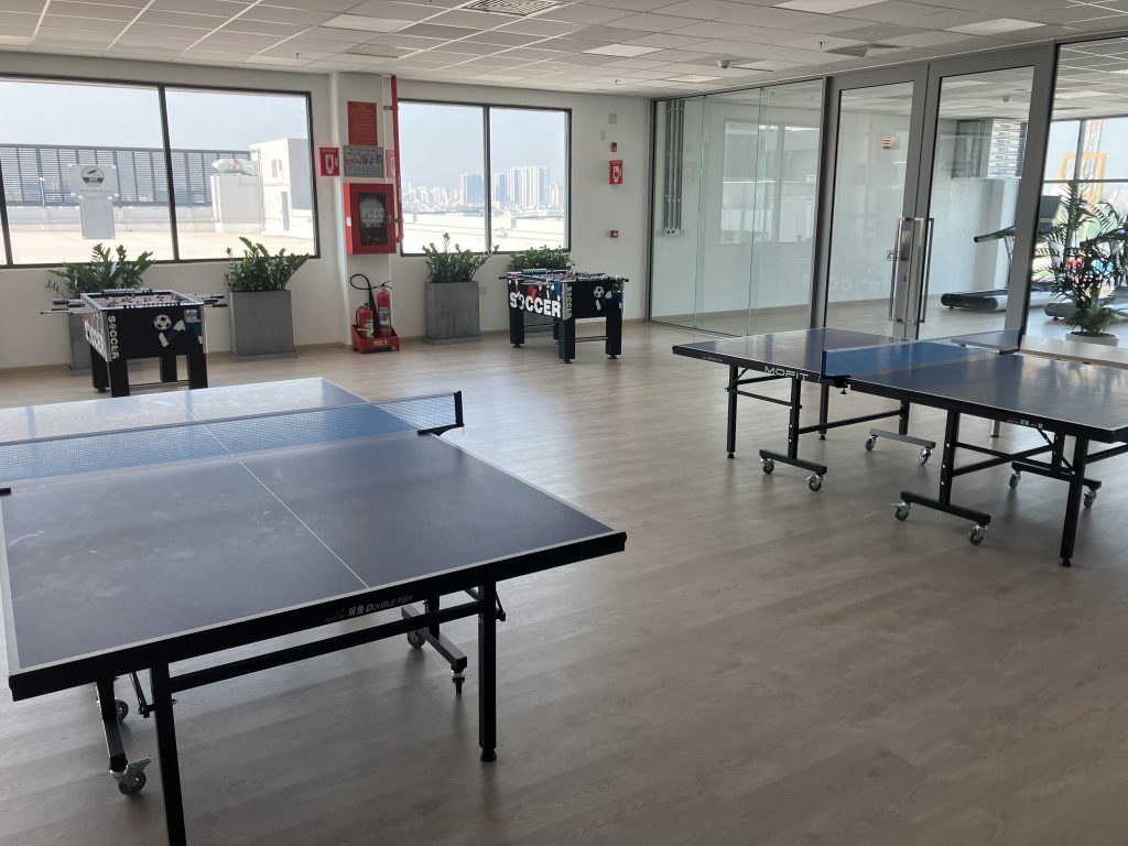 View into the light-flooded hobby room. At the front of the picture you can see two table tennis tables, at the back by the windows there are two table football tables. Adjacent to this, go through the door on the right into the fitness area.