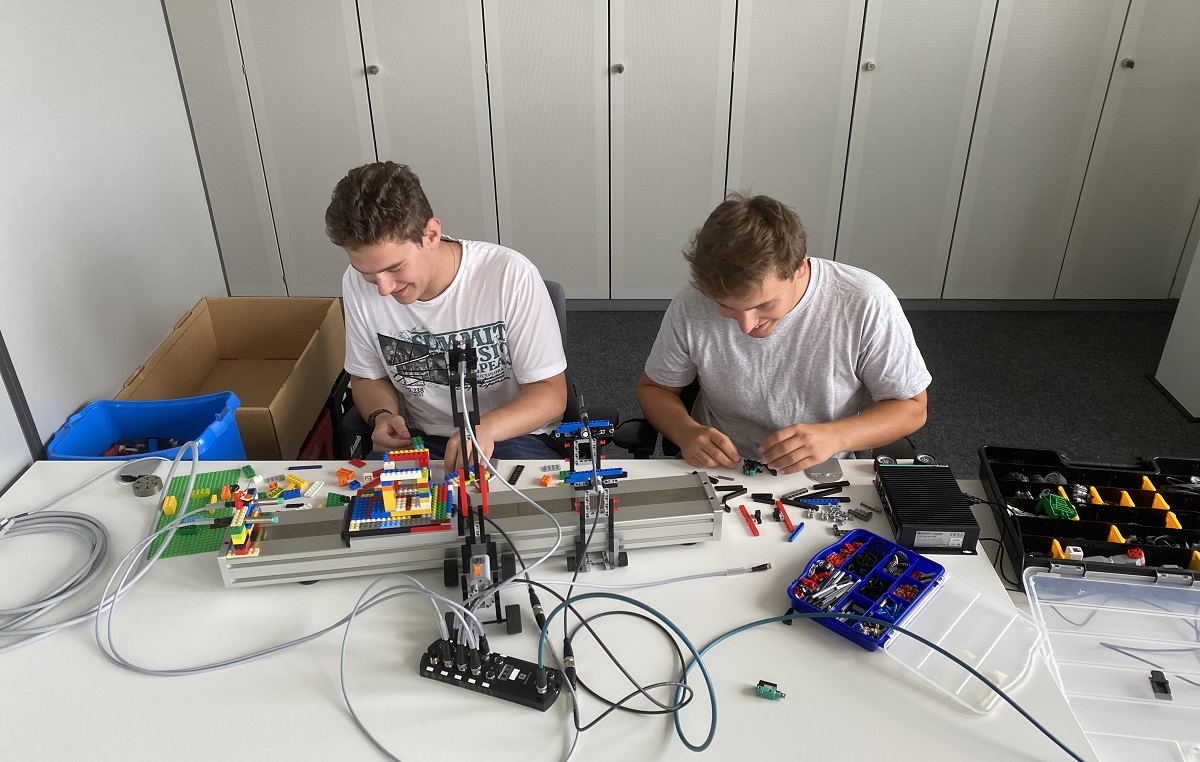 Aaron and Fabian, who are both studying electrical engineering at Pepperl+Fuchs, are sitting at the table and building their design. There are various materials on the table, including Lego blocks.