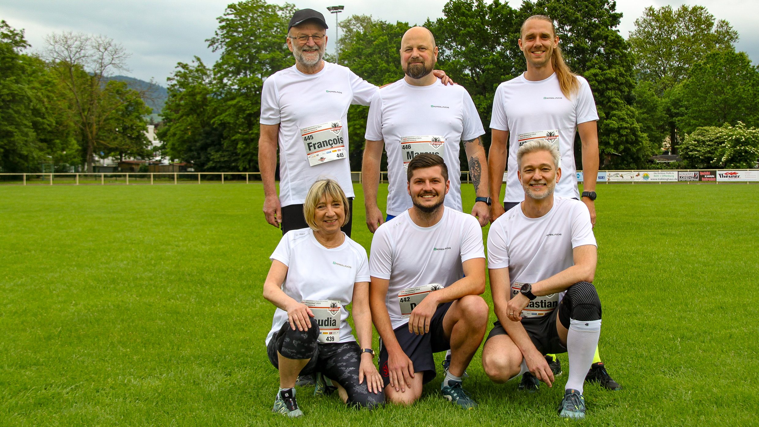 Group photo of the Pepperl+Fuchs runners at the company run in Bühl. They are on a sports field, three of them standing, the other three kneeling in front of them. They wear the white Pepperl+Fuchs running shirts.