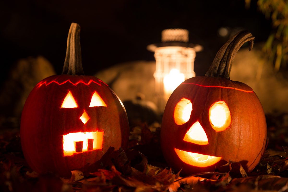 Zwei ausgehöhlte Halloween-Kürbisse mit einer Kerze im Inneren, schauen einem mit ihrem ausgeschnitzten Gesicht an.