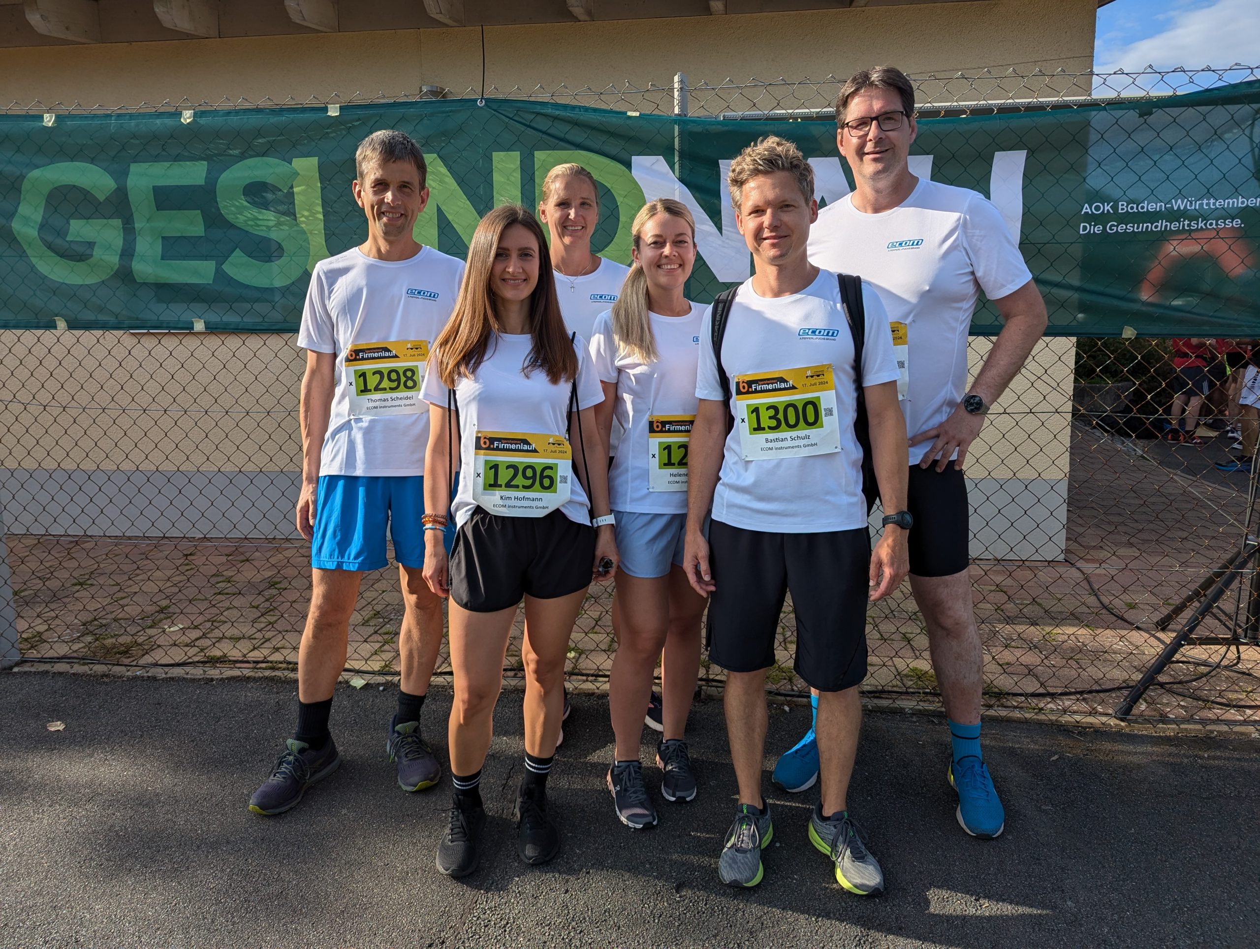 Gruppenfoto der Kolleg*innen von Pepperl+Fuchs Assamstadt beim Igersheimer Firmenlauf 2024. Die stehen auf der Straße und lächeln in die Kamera. Hinter ihnen hängt ein Banner der AOK.